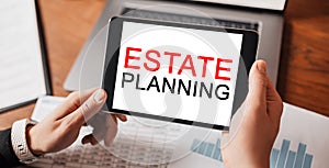 Man hands holding tablet with text Estate Planning at workplace. Businessman working at desk with documents