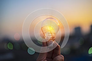 Man hands holds a house light bulb at sunset