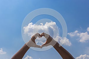 Man hands make heart shape on blue sky with clounds