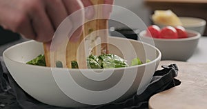 Man hands mix pesto with romaine lettuce in white bowl