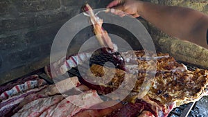 Man hands moving around pieces of beef meat in Argentinian asado to cook evenly