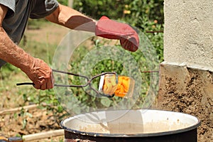 Man hands, one with red glove, holding an old canning jar lifter, drawing a jar with apricot slices out of boiling water