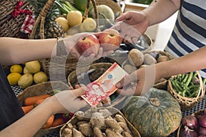 A man hands over a 50 peso bill to pay for two apples. Buying fruits at a small market stall