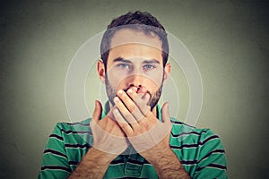 Man with hands over his mouth, speechless isolated on gray wall background