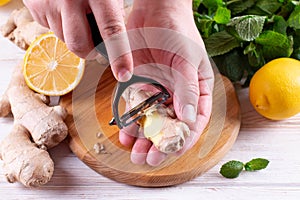 Man hands peeling fresh ginger root with knife on wood table photo