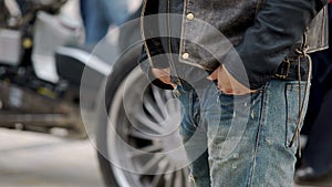 Man with hands in pockets of ripped jeans standing next to motorcycle, biker