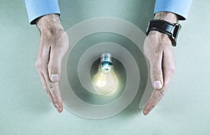 Man hands protect light bulb. Saving electric energy