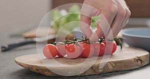 Man hands put cherry tomatoes branch on olive wood board