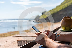 Man hands with smartphone on blurred beach background