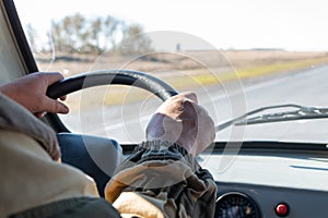 Man hands on the steering wheel of an old SUV . There are road ahead and steppe behind the windshield