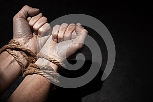 Man with hands tied with rope on black background. The concept of slavery or prisoner. Copy space for text.