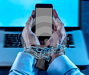 Man hands tied to mobile phone with chain padlock in internet or social media addiction
