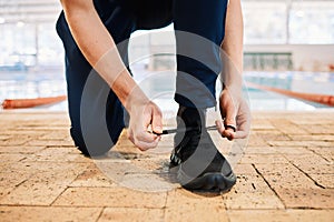 Man, hands and tying shoes by pool for workout, exercise or training preparation indoors. Closeup of male person or