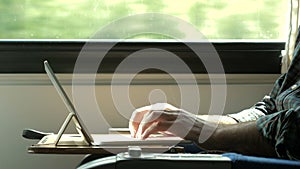 Man hands typing on laptop tablet computer in a train.