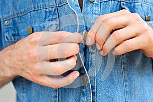 Man hands unbuttoning denim blue shirt