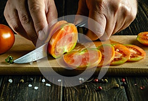 A man hands use a knife to cut tomatoes into small pieces for a vegetable breakfast dish. Tomato diet concept for vitamin set