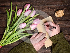 Man hands writing on blank paper sheets on old wooden table bunch of flowers on the table. Top view. Toned image.