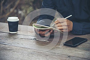 Man hands writing notebook diary with coffee cup and smartphone on wood desk. Close up man hands using pen sitting at wooden table