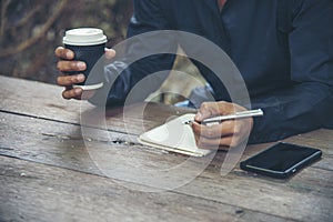 Man hands writing notebook diary with coffee cup and smartphone on wood desk. Close up man hands using pen sitting at wooden table