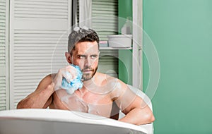 Man handsome muscular guy relaxing in bath. Spa wellness concept. Taking bath with soap suds. Treating yourself with hot