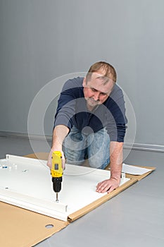 A man, a handyman in a blue jumpsuit, is assembling a table in close-up. He gathers the table frame with a screwdriver