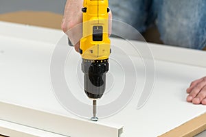 A man, a handyman in a blue shirt, collects a table, close-up. He assembles the table frame with an electric screwdriver while