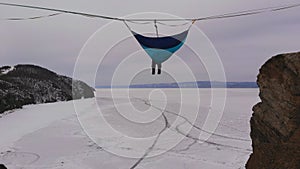 Man hanging in hammock above by ice of frozen lake Baikal.