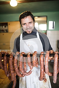 Man hanging homemade raw sausages on wooden stick.