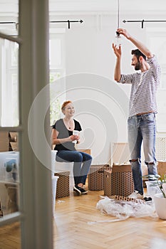 Man hanging a lamp while furnishing new home with his smiling wi