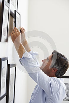 Man Hanging Picture Frames On Wall At Home