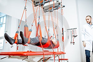 Man hanging on the suspension equipment during the spine treatment