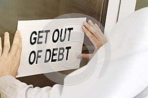 A man hangs a notice on a glass door with the text Get Out Of Debt