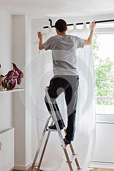 Man hangs white curtains on the curtain rod