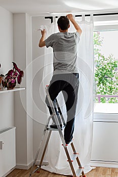 Man hangs white curtains on the curtain rod