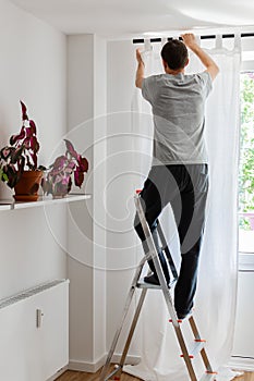 Man hangs white curtains on the curtain rod