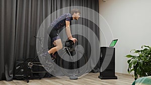 Man hard training on cycle home trainer. Male doing hard cardio exercises on smart bicycle trainer during cycling offseason at hom