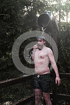 Man hardening with bucket of ice cold water after hot sauna in nature. concept of human emotions