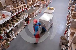 Man in hardhat working with pallet truck at warehouse, above view. Logistics center