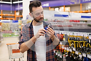 a man in a hardware store next to a rack with tools selects a pair of pliers and pliers, the concept of home repair and