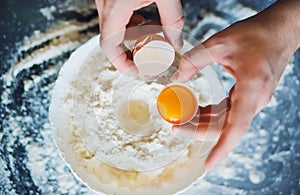 A man has broken a chicken egg and is going to mix it with flour in a bowl to make dough