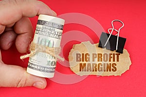The man has dollars in his hands, on a red surface there is a cardboard sign with the inscription - Big Profit Margins