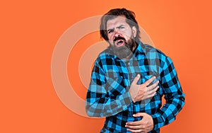 man has heartache on orange background. brutal bearded hipster feel pain. mature guy with moustache on face. expressing