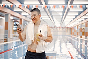 Asian man standing in indoors swimming pool and using a phone photo