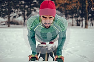 Man with a hat doing push ups on park bench in the snow