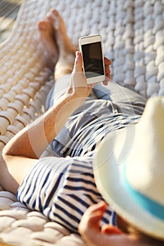 Man in hat in a hammock with mobile phone on a summer day