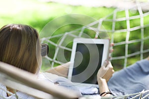 Man in hat in a hammock with tablet computer on a summer day