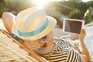 Man in hat in a hammock with tablet computer on a summer day