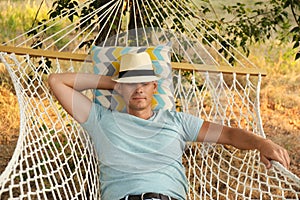 Man with hat resting in comfortable hammock at green garden