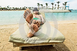 The man in the hat sunbathes on a lounge chair on the beach at a