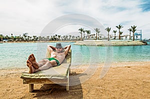 The man in the hat sunbathes on a lounge chair on the beach at a